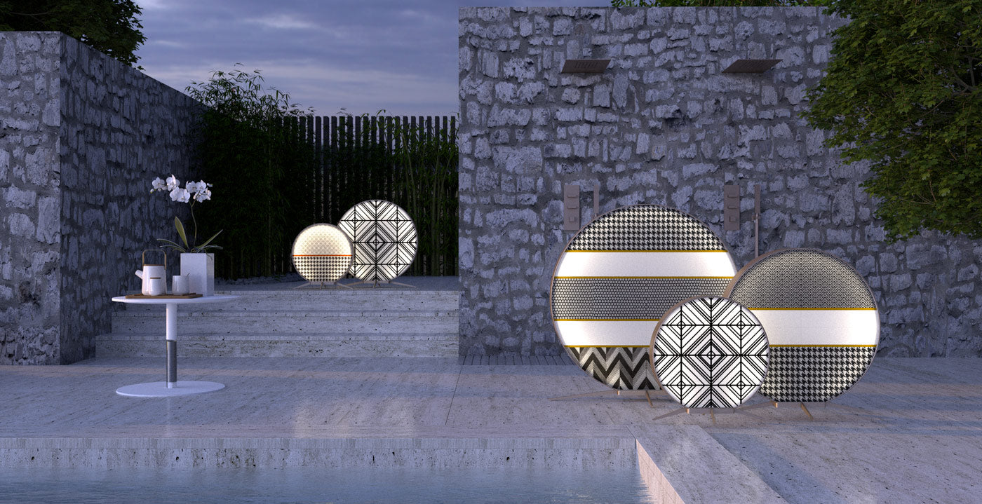 Grafika przedstawia designerskie lampy zewnętrzne postawione na modernistycznym tarasie. Lampy są przed kamiennymi ścianami.